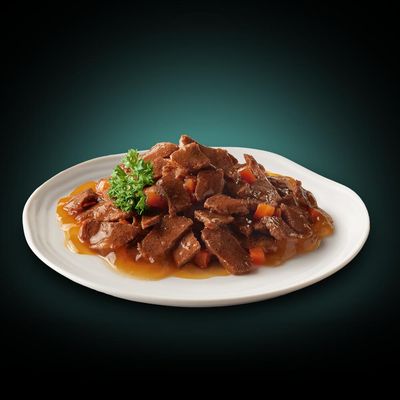 Närbild av en tallrik med köttbitar i sås, garnerad med persilja och grönsaksbitar.