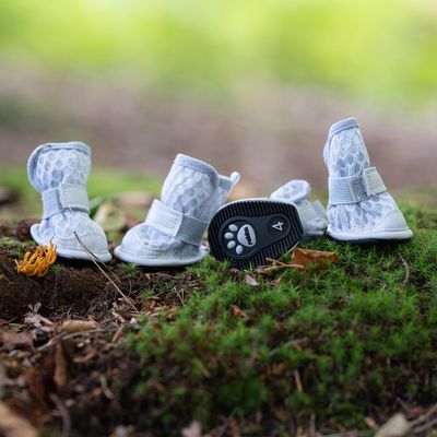 Négy fehér kutyacipő csúszásmentes talppal és mancs mintával, 4-es méret, erdei talajon elhelyezve.