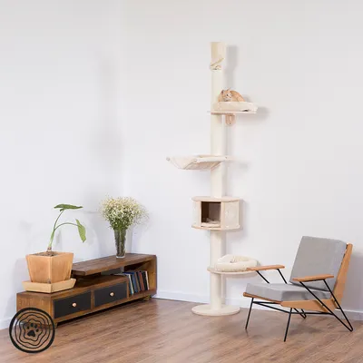 Cat tree with multiple levels, resting areas and a cave made of light wood and fabric. Placed in a modern living room with wooden furniture and plants.