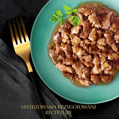 Talerz z kawałkami mięsa w sosie, udekorowany pietruszką. Tekst: MISTRZOWSKO PRZYGOTOWANE RECEPTURY.