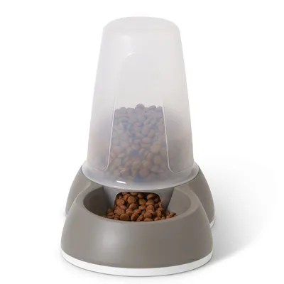 Distributore di cibo grigio con contenitore trasparente, riempito con crocchette marroni. Erogazione automatica nella ciotola sottostante.
