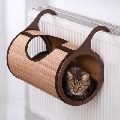 Lit pour chat en bois et tissu, fixé à un radiateur. Un chat est assis à l'intérieur du lit.