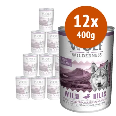 Wolf of Wilderness Wild Hills, confezione 12x400g. Lattine con etichetta viola, scritta '100% grain-free', immagine di lupo e paesaggio montano. Testo in tedesco e inglese visibile.