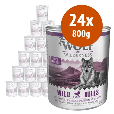 Wolf of Wilderness Wild Hills Senior, 24x800g, 100% grain-free. Confezione di lattine con anatra e vitello, frutti di bosco, radici ed erbe selvatiche. Testo in inglese e tedesco visibile.