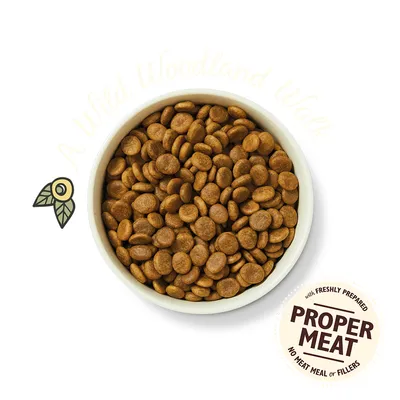 Bowl of dry pet food. Visible text: 'with freshly prepared PROPER MEAT no meat meal or fillers'. Faint background text: 'A Wild Woodland Walk'.