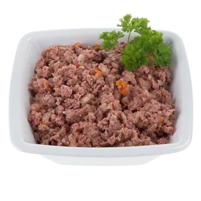 Mleta mokra hrana za hišne ljubljenčke v beli keramični posodi, na vrhu okrašena s svežim peteršiljem.