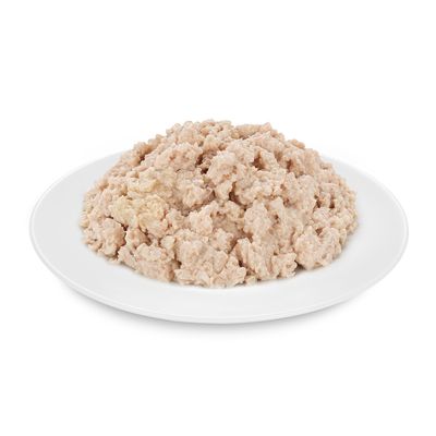 Világos színű, darabos állagú nedves állateledel fehér tányéron, csomagolás vagy márkajelzés nélkül látható.