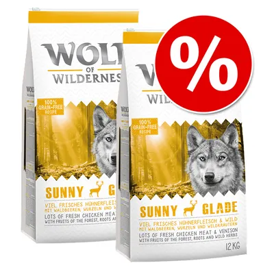 Две опаковки Wolf of Wilderness Sunny Glade, 12 кг, с етикет 100% grain-free recipe и голям червен знак за процентна отстъпка. Видим текст: lots of fresh chicken meat & venison.