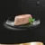 Portion of wet pet food on a black plate with a sprig of parsley garnish, shown against a dark background with water droplets. No visible brand or text.