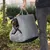 Carrier bag with grey fabric and check pattern, suitable for small dogs. Dog sits comfortably in the bag, carried by a person.