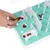 A hand places small treats in an interactive toy with obstacles and compartments on a turquoise surface.