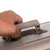 Close-up van een hand die een grijze draaggreep optilt. Toont de functionaliteit van het handvat voor transport.