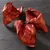 Three dried reddish-brown pig ears on a dark slate surface, shown whole with visible texture and natural shape.