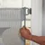 Barrière de sécurité en maille grise fixée à une porte, main tenant le bord pour l’ouvrir ou la fermer. Matériau visible : plastique et tissu.