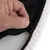 Gros plan sur une main ouvrant une fermeture éclair noire sur un tissu noir à pois et bordure beige, montrant la finition du produit textile.