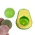 Jouet vert et jaune en forme d’avocat avec inscription « TOYS avocado », deux boules incluses, une verte et une marron tenue par une main, matériaux plastique et matière végétale visibles.