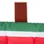 Close-up of a red-green-white striped fabric cushion with a brown felt handle on top.