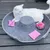 Grå filt-kattsäng med upphöjd mittdel, på den en vit katt. Leksaker: rosa boll och två rosa kuddar med mönster.