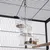 Distributeur transparent en plastique suspendu dans une cage à oiseaux, compartiments remplis de graines, marque TIAKI visible sur l’un des bacs.