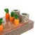Plateau en carton avec quatre carottes orange à feuilles vertes et deux cylindres en carton ondulé, tous insérés dans des trous sur la surface du plateau.
