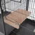 Plateforme en bois fixée par deux vis métalliques à l'intérieur d'une cage en métal noir, fond de cage visible en plastique gris foncé.