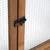 Détail d’une porte en bois avec grillage métallique et loquet noir, montrant le système de fermeture visible sur l’image.