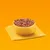 Bowl filled with dry pet food pieces and small orange chunks, placed on a yellow napkin against an orange background.