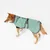 Chien portant un manteau vert clair avec fermeture à boucle et col montant, logo circulaire visible sur le côté arrière du manteau.