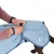 Personne attachant une sangle sur un manteau bleu clair pour chien, logo NT visible sur le côté du manteau.