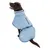 Chien marron portant un manteau bleu clair avec col montant, fermeture à boucle et poche zippée visible sur le dos. Matière textile apparente, passepoil blanc et badge rond sur le côté.