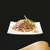 Chunks of wet pet food in gravy on a white square plate, garnished with green vegetable strips, shown against a black background.