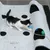 Chaton jouant sur un tapis d’activité gris Modern Living avec trous, balle verte et bleue visibles, papillon bleu attaché à une corde. Marque Modern Living imprimée sur le tapis.