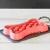Red bone-shaped feeding bowl with raised areas, filled with dry food. Placed on a grey mat next to a black and white patterned lead.