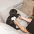 Person using an electric grooming device on a black dog lying on a sofa.