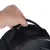 Main tenant la poignée d’un sac noir avec fermeture éclair visible, partie supérieure du sac en tissu et surface transparente partiellement visible.