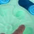 Interactive toy with green and blue surface, finger points to movable element. Promotes dexterity through hidden compartments.