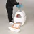 Person pouring cat litter from a blue bucket into a white automatic cat toilet with pull-out waste container. kooa brand visible on container.