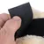 Gros plan sur une main ouvrant une fermeture à scratch noire fixée sur un tissu beige duveteux, montrant le système d’attache en plastique et textile.