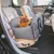 Dog sitting in a grey car seat shell with safety belts on the front passenger seat of a car. Product for safe transport of pets in vehicles.