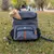 Ferplast Voyager Backpack 600, grauer Rucksack mit orangefarbenen Akzenten, geeignet für Haustiertransport. Katze sitzt im geöffneten oberen Fach des Rucksacks.