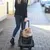 Torba transportowa na kółkach z teleskopową rączką, odpowiednia dla małych zwierząt. Kobieta ciągnie torbę po chodniku, pies siedzi z przodu torby.