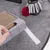 Grey felt mat with integrated scratching board made of corrugated cardboard and toy with red plush ball and grey fabric strips. Hand shows removable scratching board.