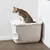 Caja de arena para gatos con tapa blanca e incorporada pala, gato sentado encima. Adecuada para uso limpio con entrada superior.