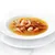 Primer plano de un bol con trozos de carne y gambas en caldo, servido en un plato blanco.