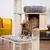 Cat tree made of wood with sisal posts, grey cushion and cave. Bengal cat climbing from the cave onto the padded platform.