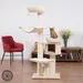 Arbre à chat en bois clair avec plusieurs plateformes, hamac, niche et coussins crème. Un chat tigré assis sur un coussin supérieur. Griffoirs en sisal visibles.