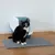 Gato negro sentado frente a un arenero cerrado con alfombrilla gris sobre suelo de madera.
