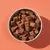 Bowl filled with brown, cube-shaped pet food treats or snacks, shown from above on a plain background.