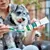 Vet's Best Dental Gel tandpasta wordt op een groene hondentandenborstel aangebracht, terwijl een hond op de achtergrond toekijkt.