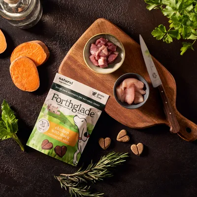 Forthglade chicken with duck natural soft bites shown with fresh sweet potato, herbs, and diced meat ingredients on a chopping board, highlighting product ingredients.
